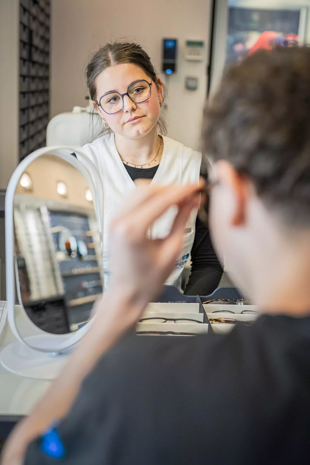 apprentie opticienne conseillant un client en train d'essayer une paire de lunettes