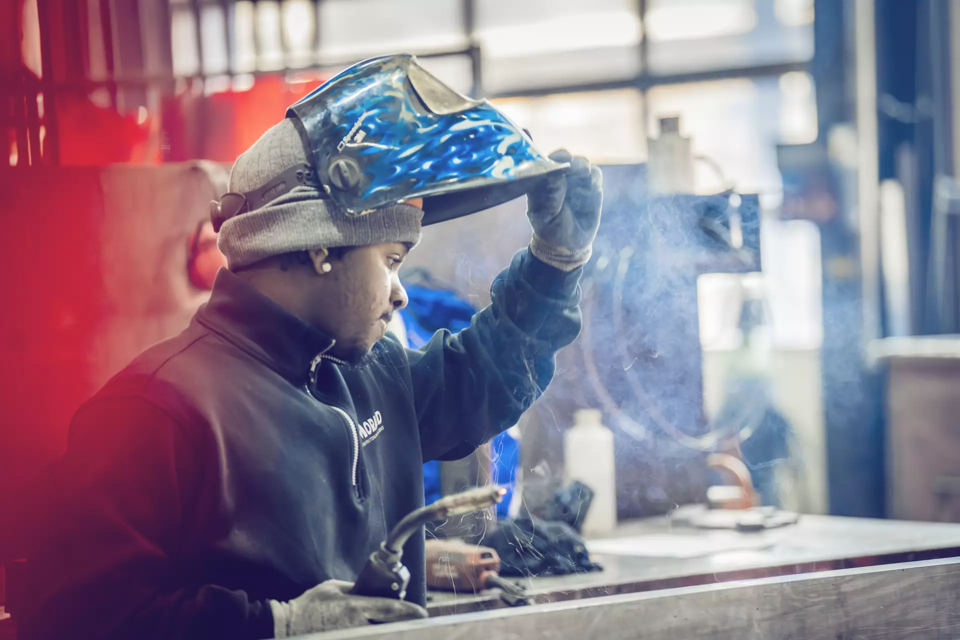 constructeur métallique faisant de la soudure relevant son casque et regardant son travail. une ombre rouge est projetée derrière lui
