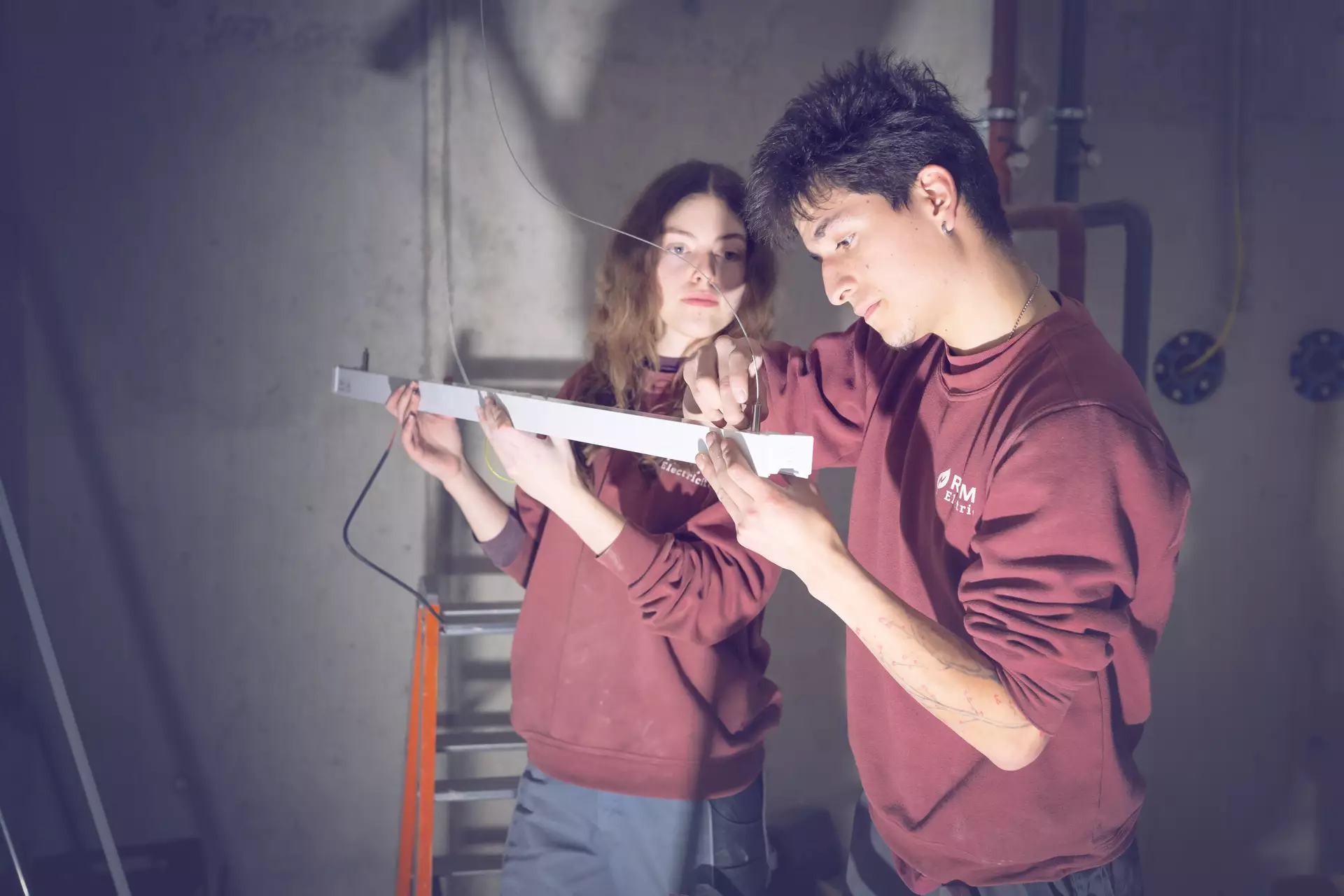 apprentie électricienne et son formateur en train de monter une lampe au plafond