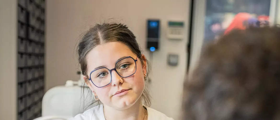 apprentie opticienne conseillant un client en train d'essayer une paire de lunettes