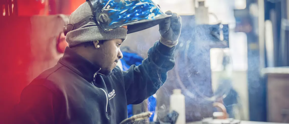 constructeur métallique faisant de la soudure relevant son casque et regardant son travail. une ombre rouge est projetée derrière lui